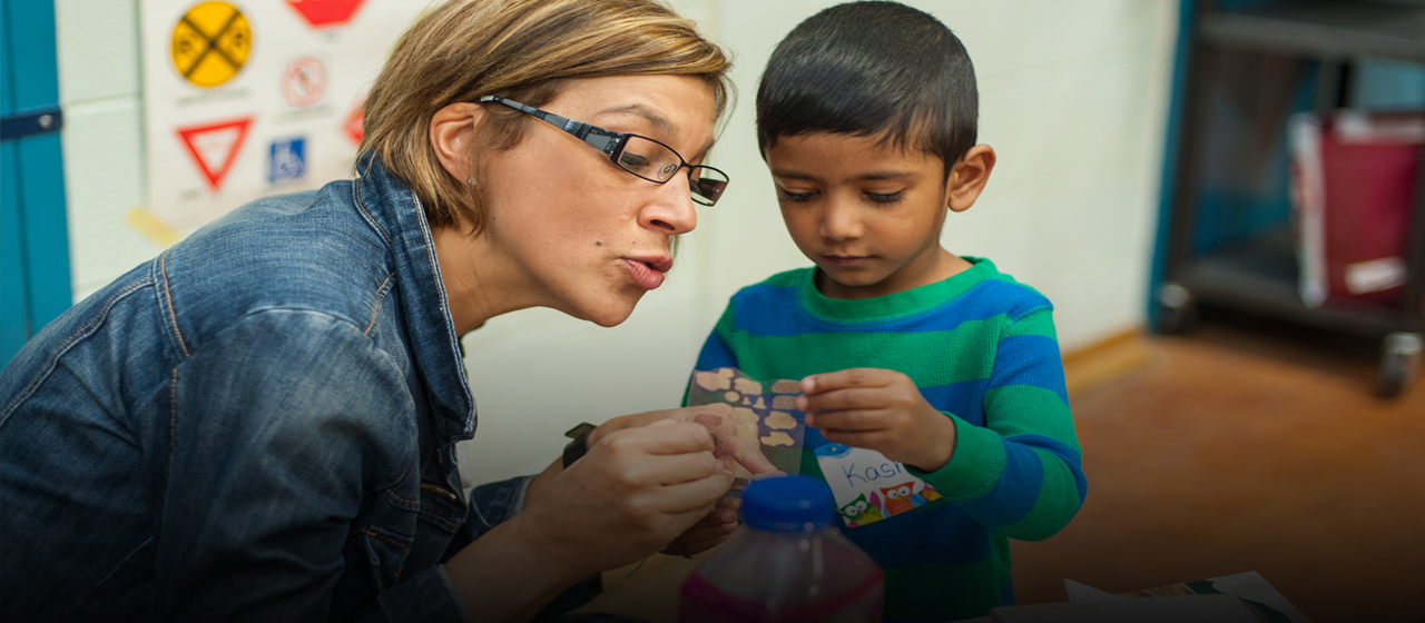 Female teacher and young boy looking closely in wonderment at child's work