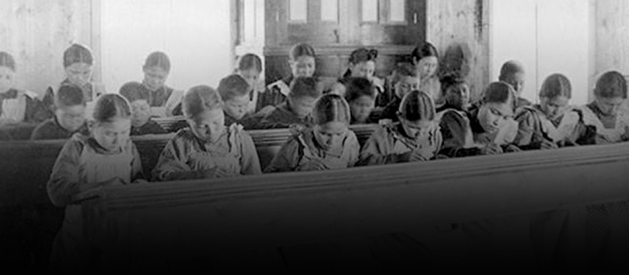 Black and white historical photo on young Indigenous girls working in rows in a residential school.